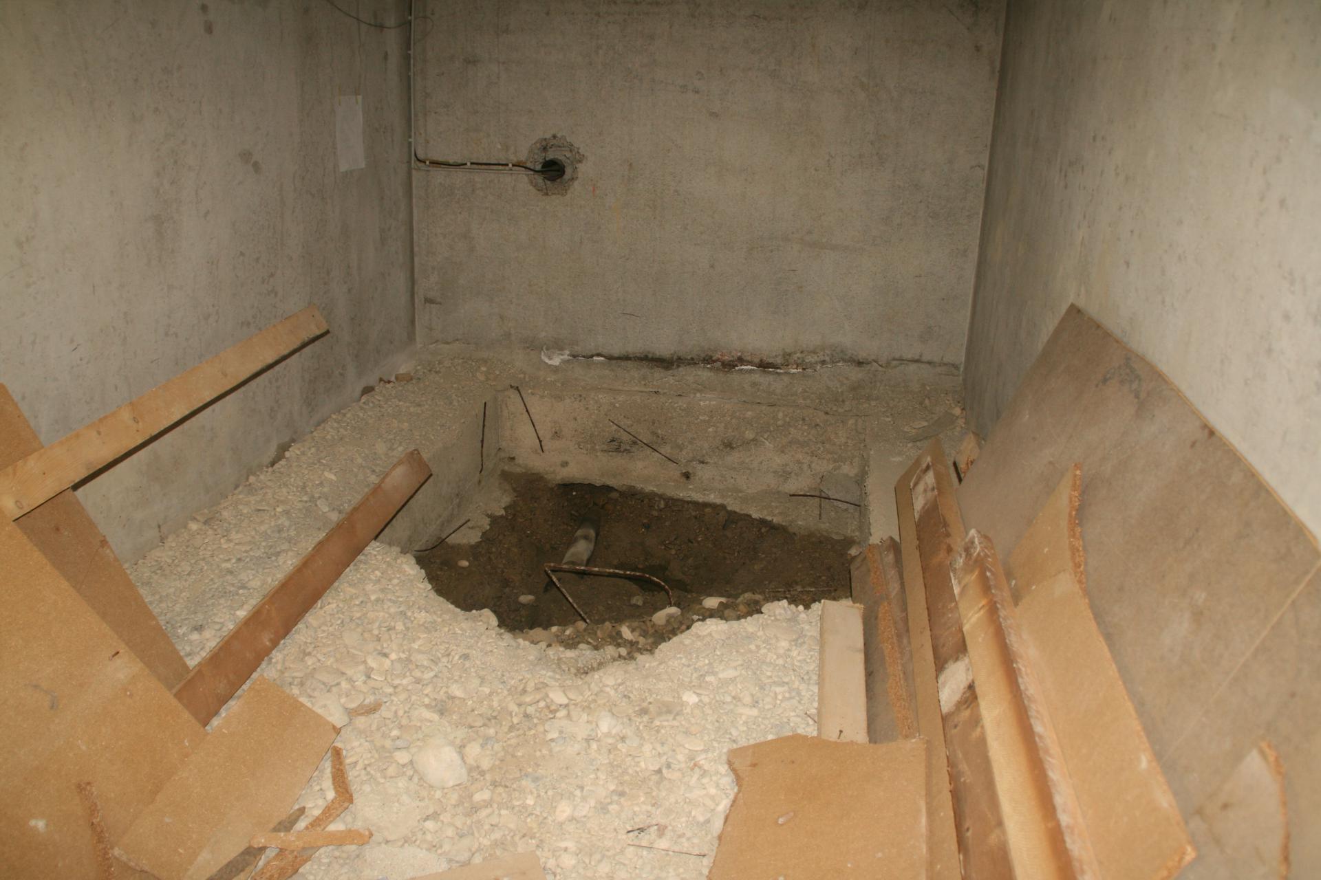 Ein etwa 2m breites, 1m tiefes Loch im Kellerboden. Man erkennt feuchten Boden und sieht auch bereits das Wasser stehen.